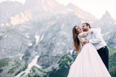 Gelin ve damat dağlardaki gölün kenarında. Yeni evliler bir dağ manzarasının arka planına karşı birlikte. Aşık romantik bir çift..
