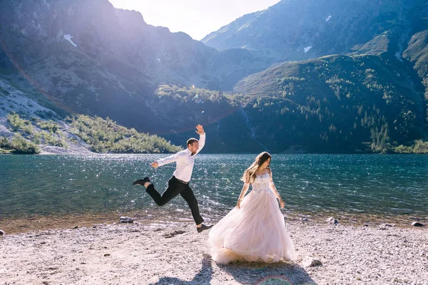 在美丽风景的映衬下 新婚夫妇在湖边跳舞 一个男人跳了起来 — 图库照片