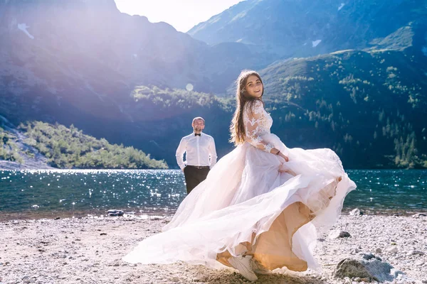 美丽而快乐的新娘 穿着一条长长的白色连衣裙 在河边的丈夫面前翩翩起舞 — 图库照片