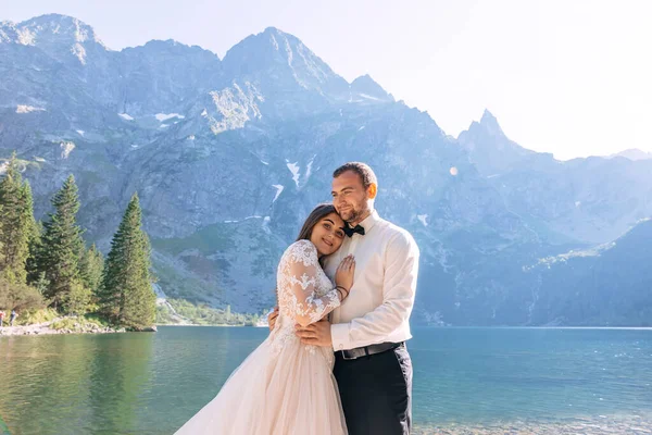 Νύφη Φόρεμα Και Γαμπρός Σμόκιν Αγκαλιάζονται Θέα Όμορφα Βουνά Ενώ — Φωτογραφία Αρχείου