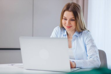 Mutlu, neşeli, pozitif, güzel iş kadını evde oturmuş laptopla çalışıyor, ders çalışıyor.