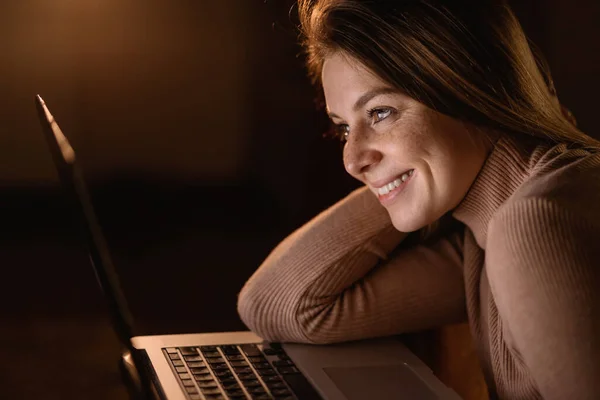 Young woman watches videos on internet on her laptop at home and smiles. Extreme close up