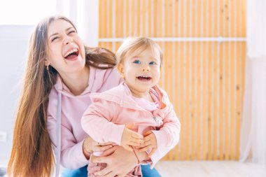 . happy mother hugs her little daughter, they smile from happiness, sitting on the floor in the room.