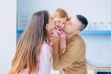 Sevgi dolu anne ve babalar mutlu bir kız evlat tutarlar, yanaklarından öpüşürler..