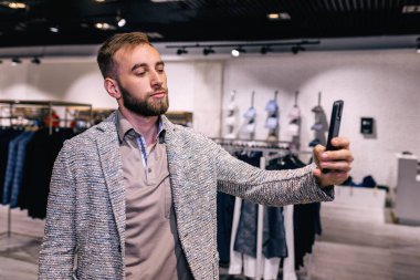 Adam giyim mağazasında selfie çekiyor.