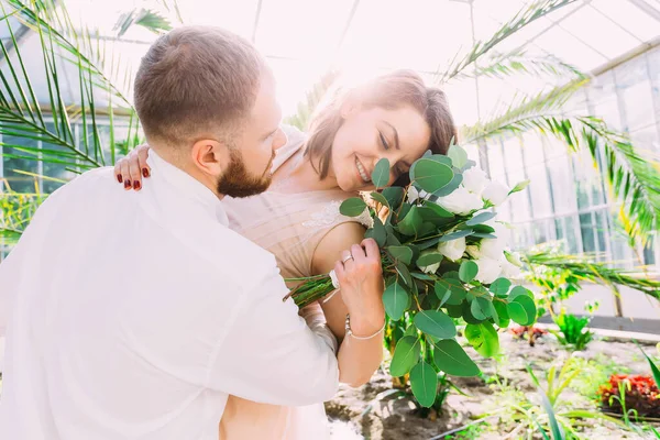 幸福的新婚夫妇 在一个玻璃植物园里 一个女孩拿着一束鲜花 — 图库照片