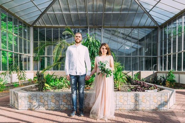 新娘和新郎走在靠近古老玻璃建筑的植物园里 手牵着手 — 图库照片
