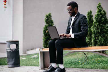 Bir üniversite öğrencisi kampüste bir bankta oturur ve dizüstü bilgisayarla çalışır..