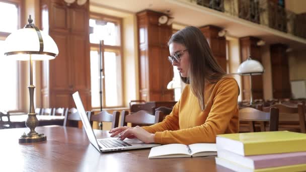 Kobieta Okularach Swetrze Uczy Się Przy Stole Bibliotece Używając Laptopa — Wideo stockowe