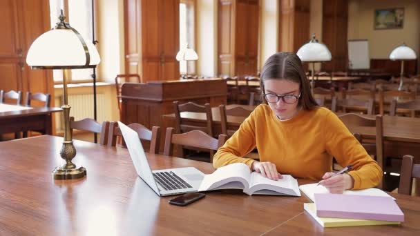 Piękna Mądra Dziewczyna Okularach Pomarańczowym Swetrze Siedzi Bibliotece Dla Podręczników — Wideo stockowe
