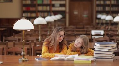 Öğretmen çocuğa yazmayı, okumayı öğretir, çocuk okul kütüphanesinde ders çalışır.