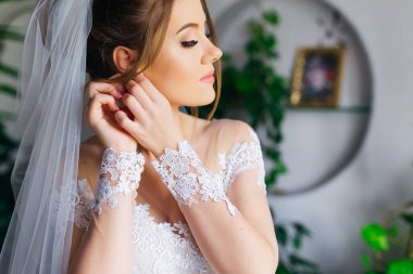 Sensual morning preparation of a young beautiful bride. a gentle bride in a dress puts on earrings. Bride with luxurious hair and makeup.