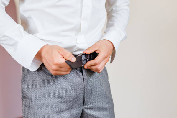 man putting on brown belt on his trousers, cropped shot