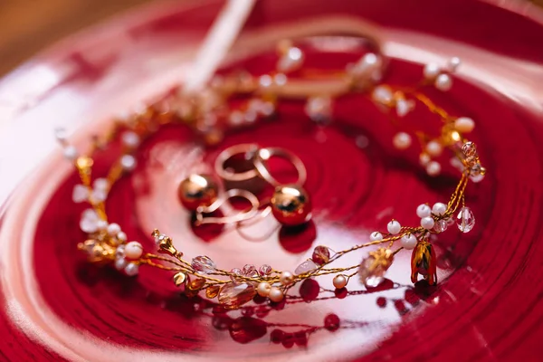 ダイヤモンドイヤリングおよび結婚指輪は赤い板のTiaraとある 結婚式の詳細 — ストック写真