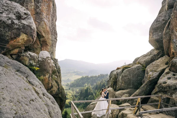 在岩石之间的群山中 新婚夫妇温柔而美丽的拥抱 Honeymoon 本质上的照片会话 — 图库照片