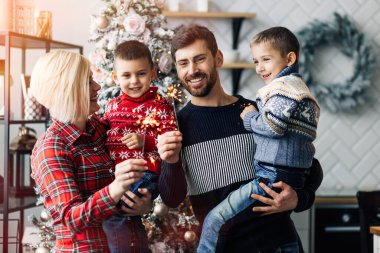 Anne, baba, Noel 'de evde havai fişeklerle poz veren iki oğul dekorasyonun arka planına karşı.