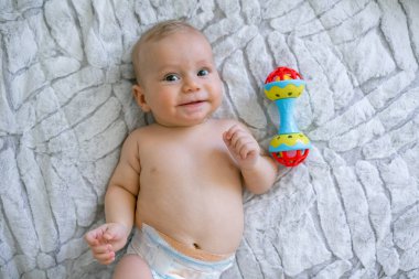 Tatlı erkek bebek gülümse ve çıngıraklı oyuncağın yanında uzan, küçük çocuk eğlen