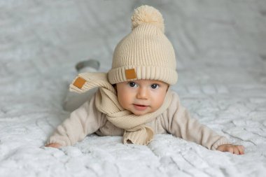 Yatakta örülmüş bir şapkayla emekleyen şirin bir bebeğin portresi.