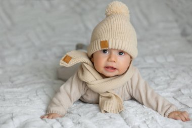 3 aylık şirin bir bebeğin portresi battaniyeye uzanmış şık örülü bir şapka ve eşarp giyiyor.
