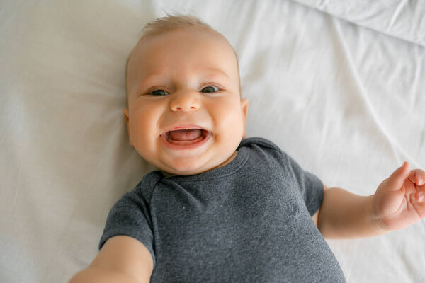 smiling newborn happy baby on a white bed at home