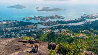 İki yürüyüşçü, turkuaz denizleri, tropikal adaları ve bereketli tepeler boyunca yayılmış bir kıyı kasabasını geniş bir açıdan görmek için kayalık bir tepede mola verir..
