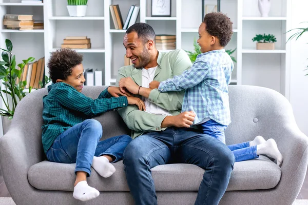 Neşeli bir aile, oturma odasındaki kanepede birlikte otururken küçük oğullarıyla eğleniyor ve oynuyor..