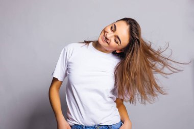 Beyaz tişört ve beyaz arka planda kot pantolon giymiş gülümseyen kadın portresi. Stüdyo. Dalgalı saç.