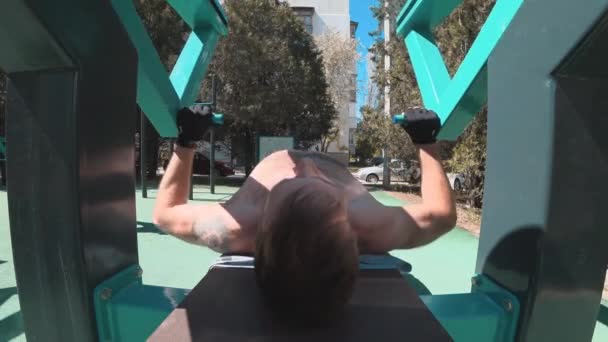 Молодой парень отжимает скамейку на тренера на открытом воздухе — стоковое видео