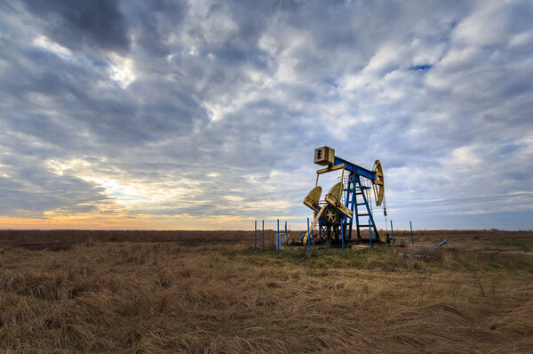 Operating oil and gas well profiled on sunset sky