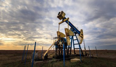 Operating oil and gas well profiled on sunset sky clipart
