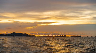 İthalat için büyük kargo gemileri ihracat kargoları. Akşamları deniz açıklarında altın bir günbatımıyla demir atıyorlar..