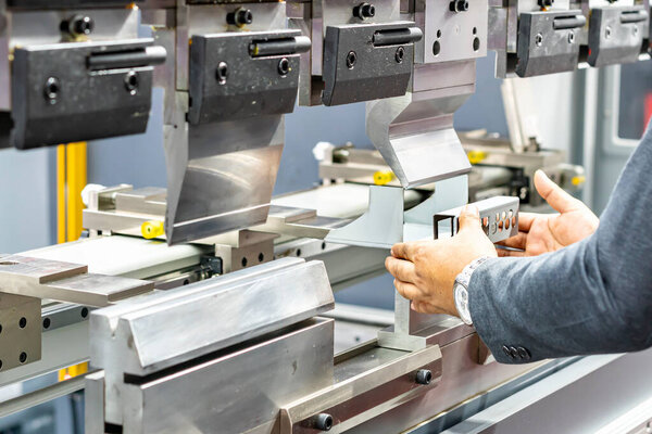 Close up teeth of the semi automatic hydraulic bending machine and the technician's hands catch the metal sheet or the workpiece during folding forming.