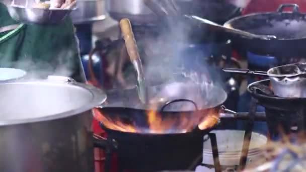 Шеф-повар стрит-фуда готовит на черной сковороде с огнем на улице Йохадж Роуд Бангкок Таиланд — стоковое видео