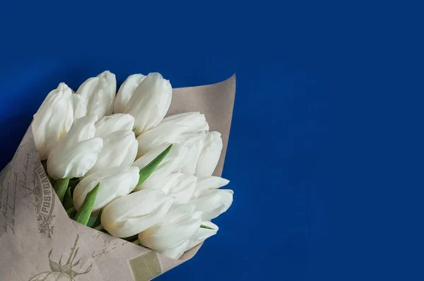 A bouquet of white tulips covered into vintage brown paper. Blue background. — Stock Photo, Image