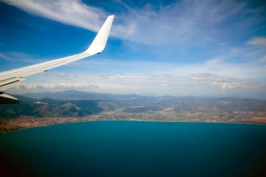 Sonsuz denizin üzerinde uçan uçak kanadı manzarası. Güneşli yaz gününde arka planda kıyı.