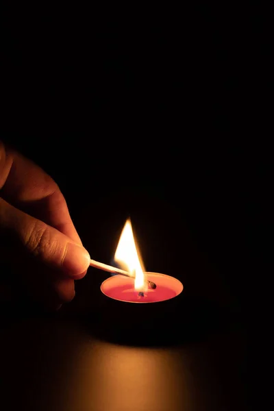 Acendendo uma vela vermelha com um fósforo no escuro. Conceito de memória. Fundo preto, orientação vertical. — Fotografia de Stock