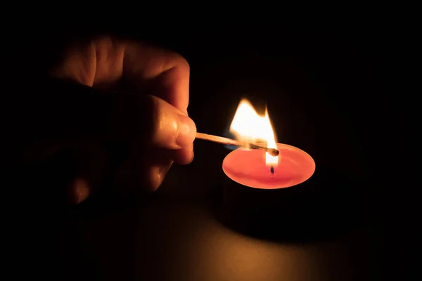 Acendendo uma vela vermelha com um fósforo no escuro. Conceito de memória. Fundo preto. — Fotografia de Stock