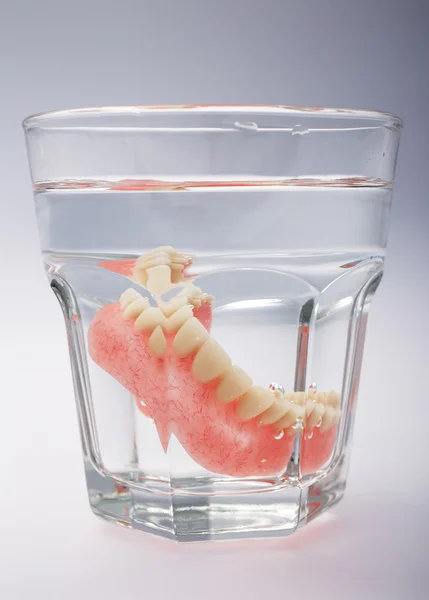 Um conjunto de dentaduras em um copo de água — Fotografia de Stock