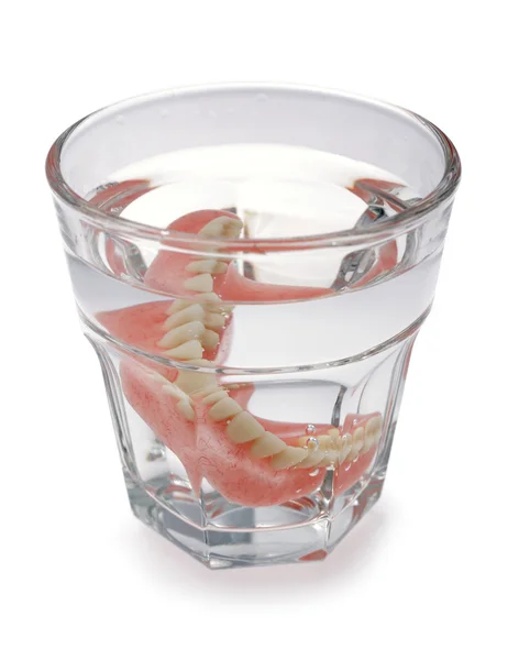 Um conjunto de dentaduras em um copo de água — Fotografia de Stock