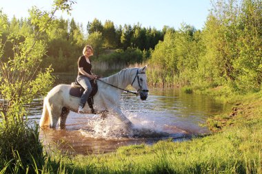 Elderly woman on a white horse in a pond enjoying a beautiful day-Concept of love between people and animals-Horse is a noble animal