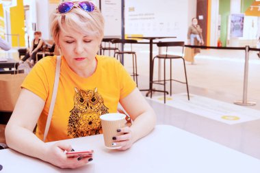 Genç ve güzel bir kadın kahve içiyor ve telefonda konuşuyor.