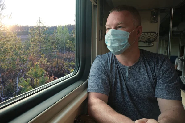 A man in a medical mask rides by the window on a train — Stock Photo, Image