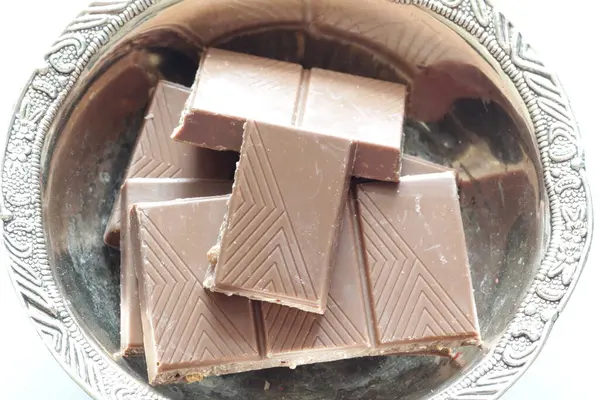 Melk chocolade stukken in de kom op blauwe achtergrond van bovenaf bekijken. Sluit een chocoladereep op blauwe achtergrond. — Stockfoto