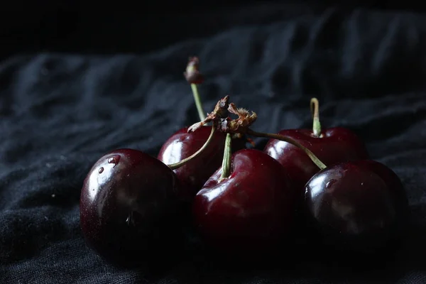 Свежие сладкие спелые вишни на деревенской тарелке на черном фоне. Закрыть. — стоковое фото