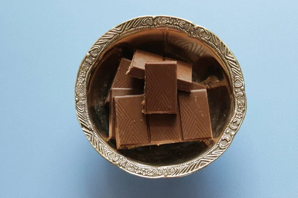 Melk chocolade stukken in de kom op blauwe achtergrond van bovenaf bekijken. Sluit een chocoladereep op blauwe achtergrond. — Stockfoto