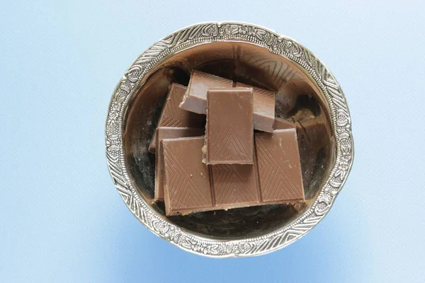 Mléčná čokoláda kousky v misce na modrém pozadí z horního pohledu. Zavřít čokoládovou tyčinku na modrém pozadí. — Stock fotografie
