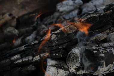 Yanmış odunlar yakın çekim ateşinde yanmış. Atmosferik arka plan ve kamp ateşi. İçeriden kopyalanmış şenlik ateşinin tasavvur edilemez detaylı görüntüsü. Duman fırtınası ve parlayan közler..