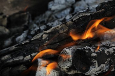 Yanmış odunlar yakın çekim ateşinde yanmış. Atmosferik arka plan ve kamp ateşi. İçeriden kopyalanmış şenlik ateşinin tasavvur edilemez detaylı görüntüsü. Duman fırtınası ve parlayan közler..