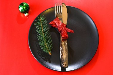 Noel masası siyah tabakta, kırmızı masada yeşil top, kopyalama alanı. Noel yemeği, parti tasarımı, konsept. Üst görünüm.