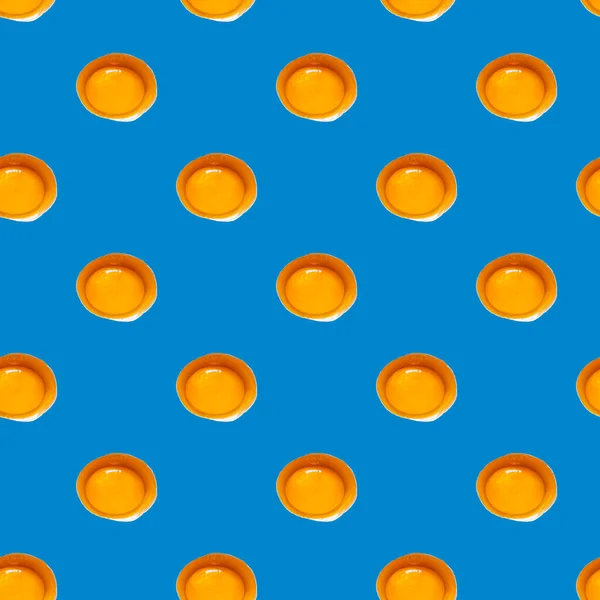 Seamless pattern of raw yellow eggs yolks on a blue background. Broken egg repeating ornament backdrop, Easter banner.